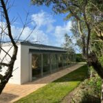 Alcino Soutinho's Soutinho 14 Villas no Bom Sucesso at Bom Sucesso Resort, Obidos, showcasing modern homes with grass landscaping, shrubs, and garden buildings in a well-shaded yard.