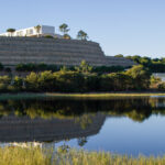 Alcino Soutinho's design of the Soutinho Conjunto de 28 Habitações em Banda at Bom Sucesso Resort, Obidos, showcasing a panoramic view with a blue sky and surrounding landscape including a reservoir and wetland.