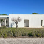 Álvaro Siza Vieira's Siza 14 Villas no Bom Sucesso at Bom Sucesso Resort, Obidos, showcasing a modern concrete structure with a composite material façade, surrounded by grass and shrubs.